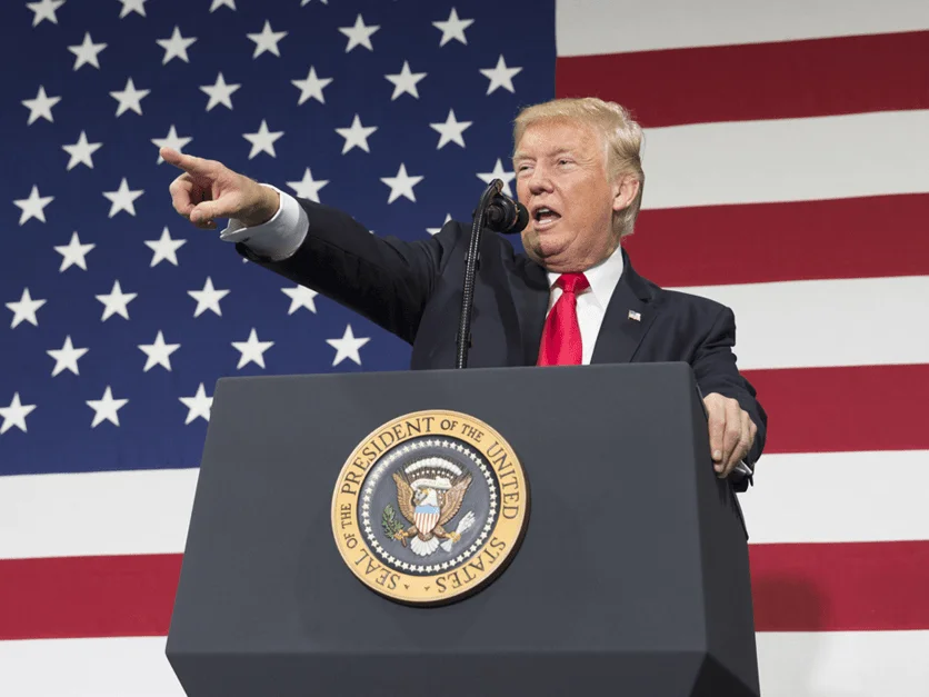 Donald Trump speaking at a lectern in front of American flags